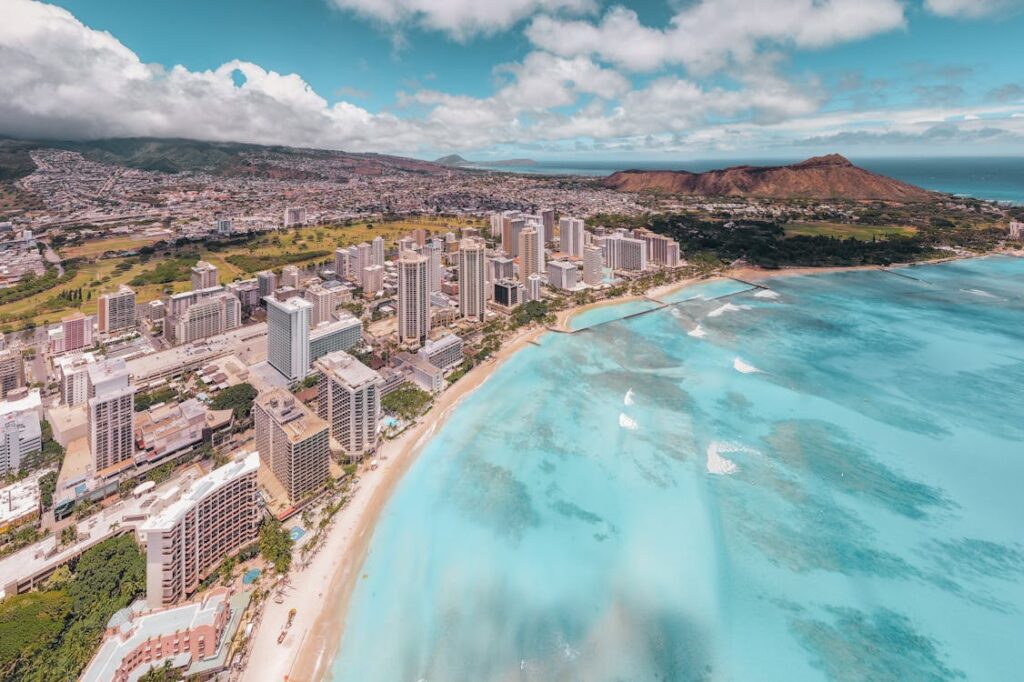 Family enjoying a summer vacation on a sandy beach in Honolulu, Hawaii, building sandcastles and playing in the shallow waves, with palm trees and a clear blue sky in the background.