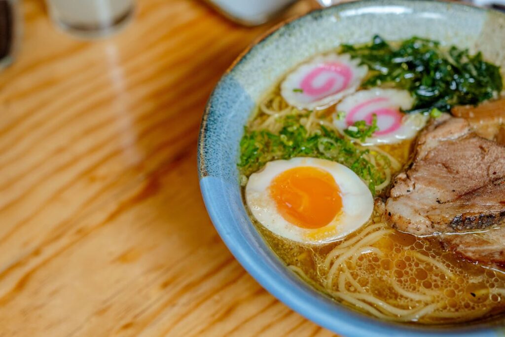 Adding toppings to ramen: arranging soft-boiled egg, green onions, meat slices, and seaweed on noodles in a bowl