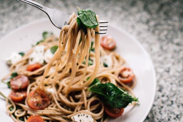 "A detailed step-by-step image showing the process of making homemade spinach spaghetti. The photo captures fresh spinach being blended into a puree, then mixed with flour and eggs on a wooden surface to form dough. The dough is rolled out and cut into thin spaghetti strands, ready to be cooked. This visual guide emphasizes the homemade aspect and the unique green color of the spinach-infused spaghetti."