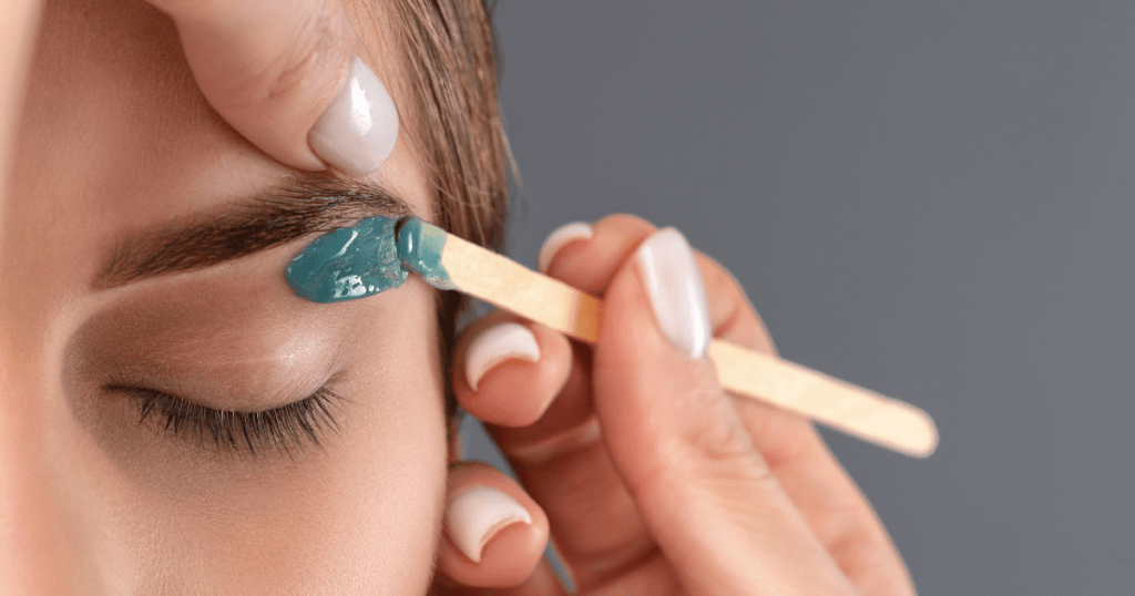 A professional cosmetologist performing a precise brow waxing treatment on a client, using high-quality wax and tools to shape and define the eyebrows perfectly.