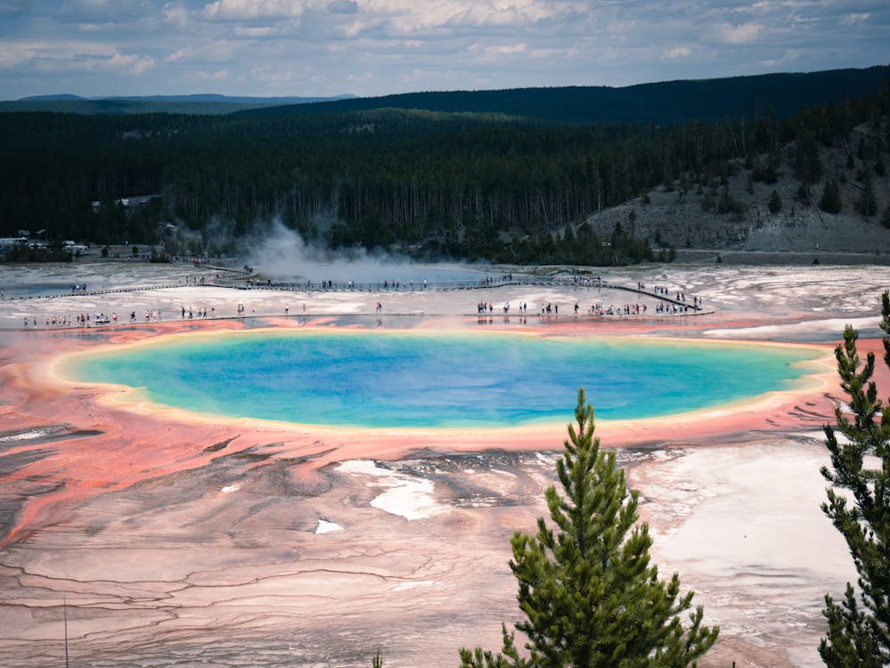 Family enjoying a summer vacation at Yellowstone National Park, Wyoming, observing the famous Old Faithful geyser erupting on a sunny day, with lush greenery and clear blue skies in the background.