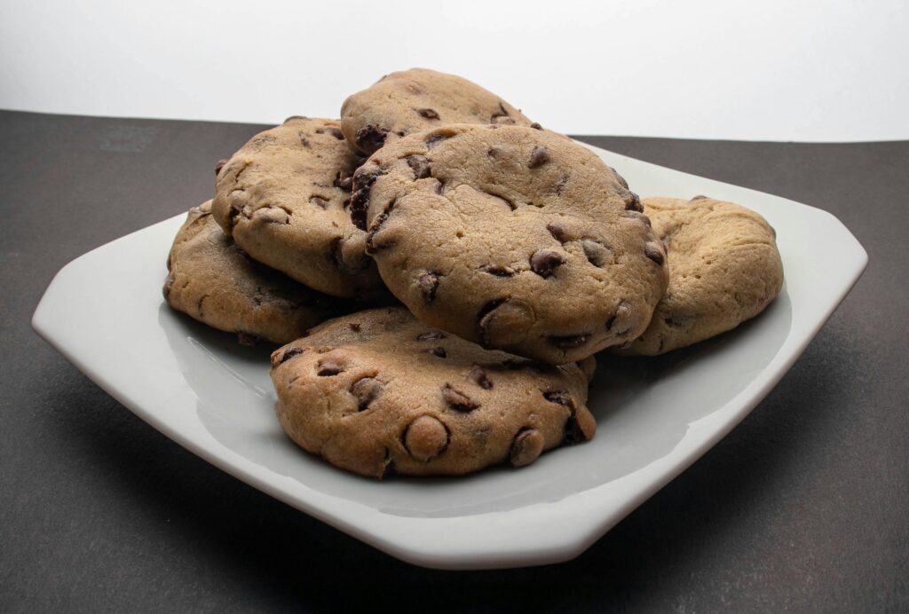 Freshly baked brown butter chocolate chip cookies, golden brown and chewy, with melted chocolate chunks and a sprinkle of sea salt on top, arranged on a rustic wooden platter.