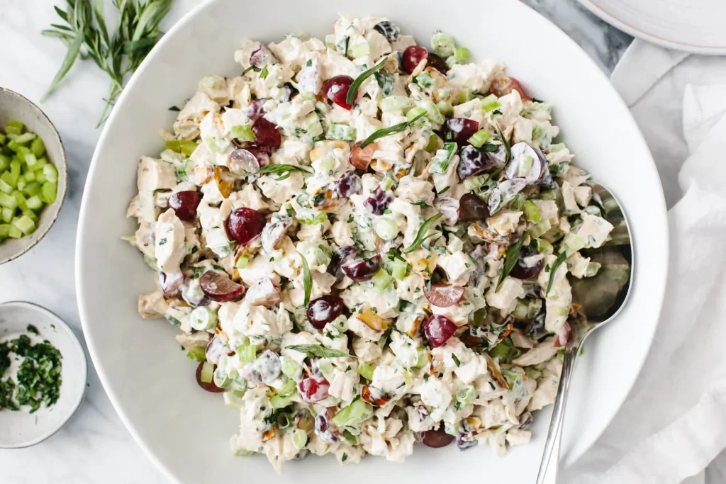 Image shows a bowl of freshly made chicken salad being mixed together, featuring tender shredded chicken, creamy mayonnaise, and a variety of chopped vegetables like celery and onions. The ingredients are being combined to create a flavorful filling, perfect for assembling a Chicken Salad Sandwich