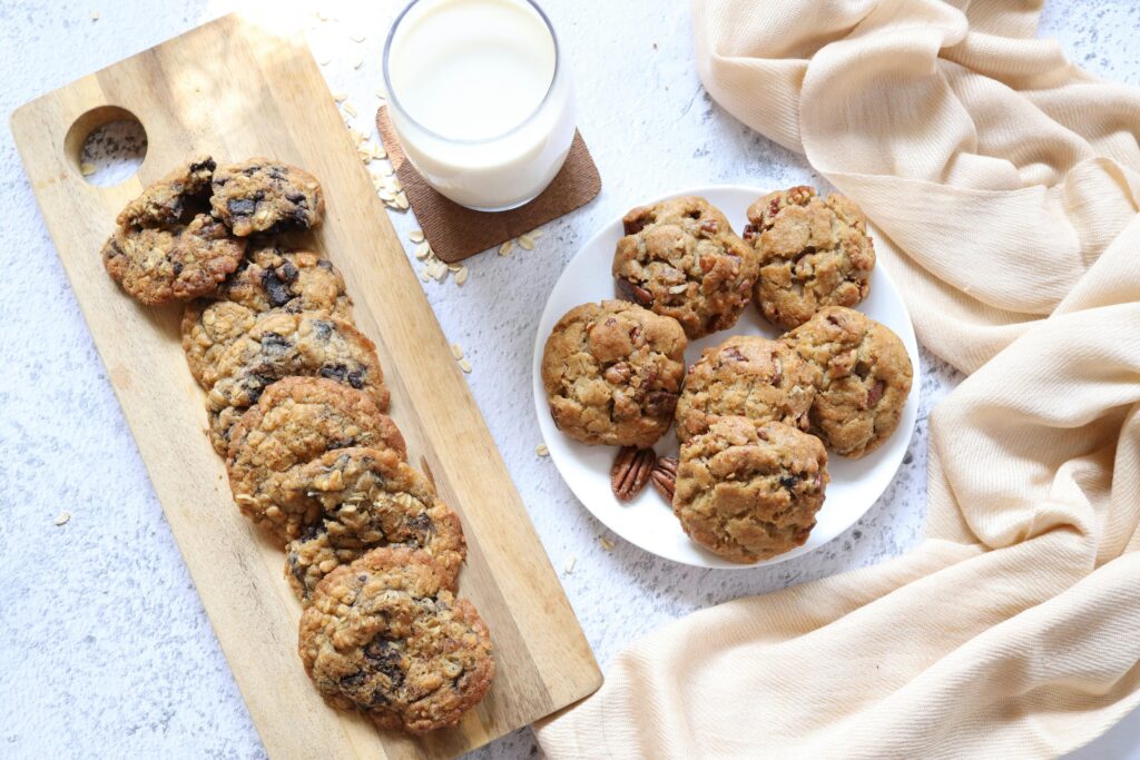 Freshly baked oats chocolate chip cookies on a cooling rack, showcasing a golden-brown exterior and chunks of dark chocolate peeking through. The cookies have a rustic texture, highlighting the addition of rolled oats, with a sprinkle of sea salt on top