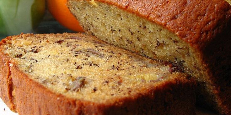 A fresh, moist banana bread made with overripe bananas sits on a wooden cutting board, its golden-brown crust lightly glistening. The inside reveals a soft, tender texture, perfect for a sweet treat. The loaf is slightly cracked on top, adding a rustic charm, while its delicious aroma fills the room.