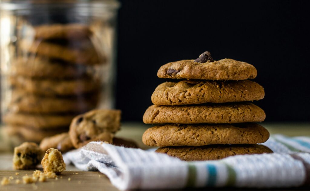 A plate of golden-brown, freshly baked peanut butter cookies with a unique twist. The cookies are perfectly round, with a soft texture and slightly crisp edges. Their rich, nutty aroma is complemented by a subtle hint of sweetness. Each cookie is topped with a light drizzle of chocolate, adding a delightful contrast to the classic peanut butter flavor