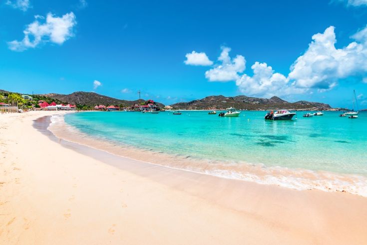 An aerial view of St. Barts, a serene gem in the Caribbean Islands, showcasing its luxury resorts nestled along pristine white-sand beaches. The turquoise waters gently lap against the island's quiet shores, offering a perfect blend of opulence and untouched natural beauty."