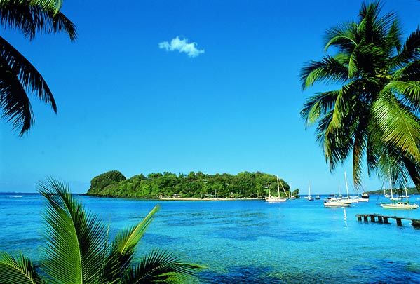 A stunning aerial view of St. Vincent & The Grenadines, a pristine paradise in the Caribbean Islands. Crystal-clear turquoise waters surround lush green islands, with a sailboat gliding between them, perfect for island-hopping adventures. The white sandy beaches stretch along the coastline, inviting relaxation and exploration. The vibrant natural beauty captures the essence of this Caribbean gem.