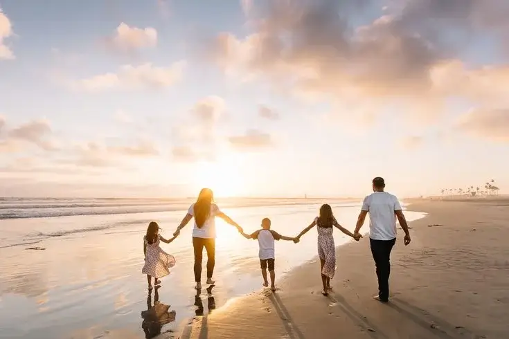 A happy family enjoying a sunny day at the beach, with colorful umbrellas, beach towels, and toys scattered on the sand. Perfect scene capturing the essence of a Family Beach Vacation, with children playing by the water and parents relaxing under the shade.